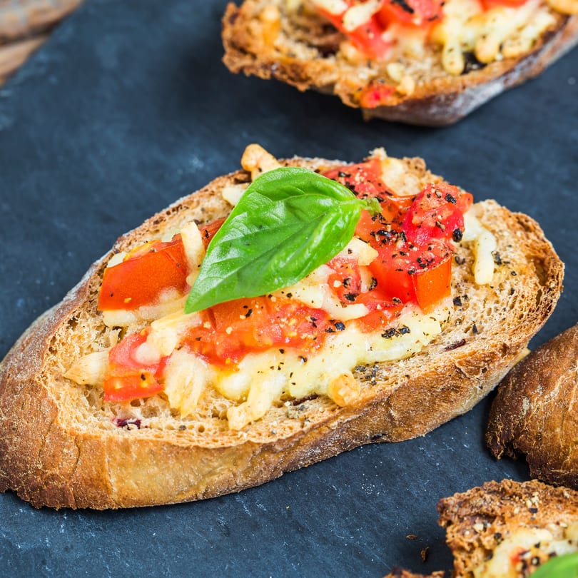 Close-up of Cestra's Pizza III bruschetta with melted cheese, diced tomatoes, pepper, and basil.