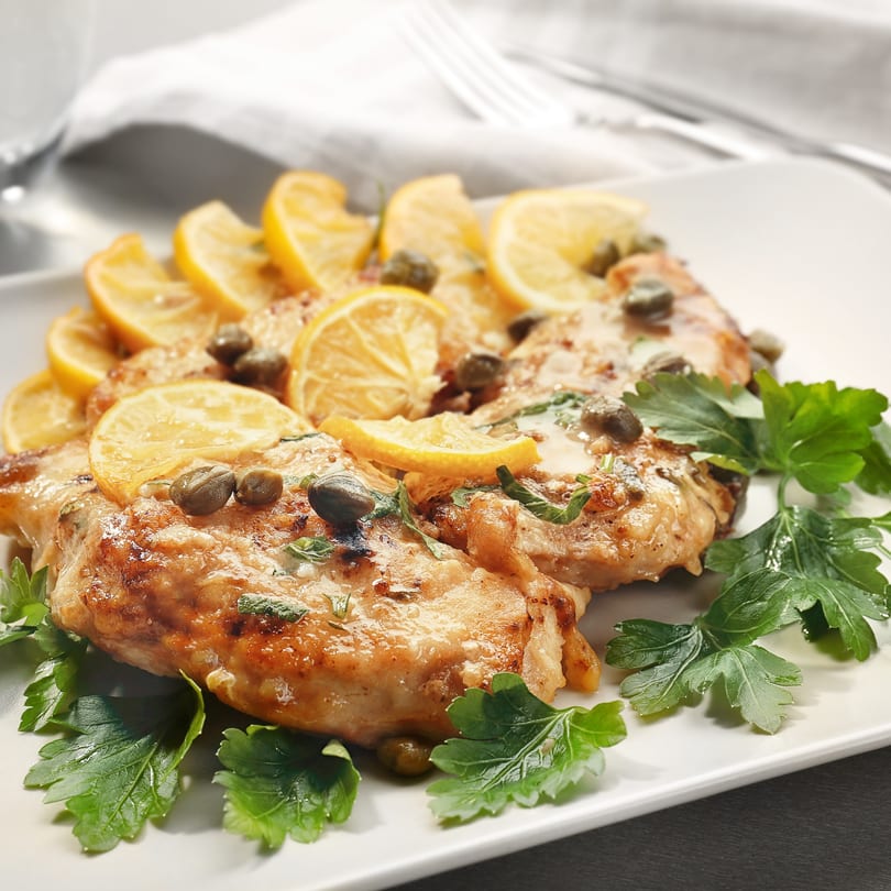 Chicken piccata with lemon slices, capers, and fresh parsley on a white plate.