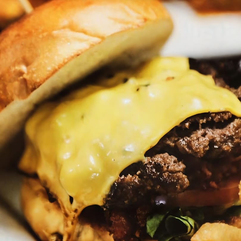 Close-up of a cheeseburger with melted cheese, two patties, lettuce, and tomato on a bun.